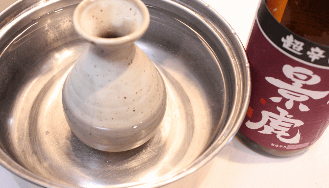 A tokkuri of sake heating up in a bowl of hot water