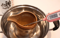 A katakuchi of sake heating up while its temperature is checked with a thermometer